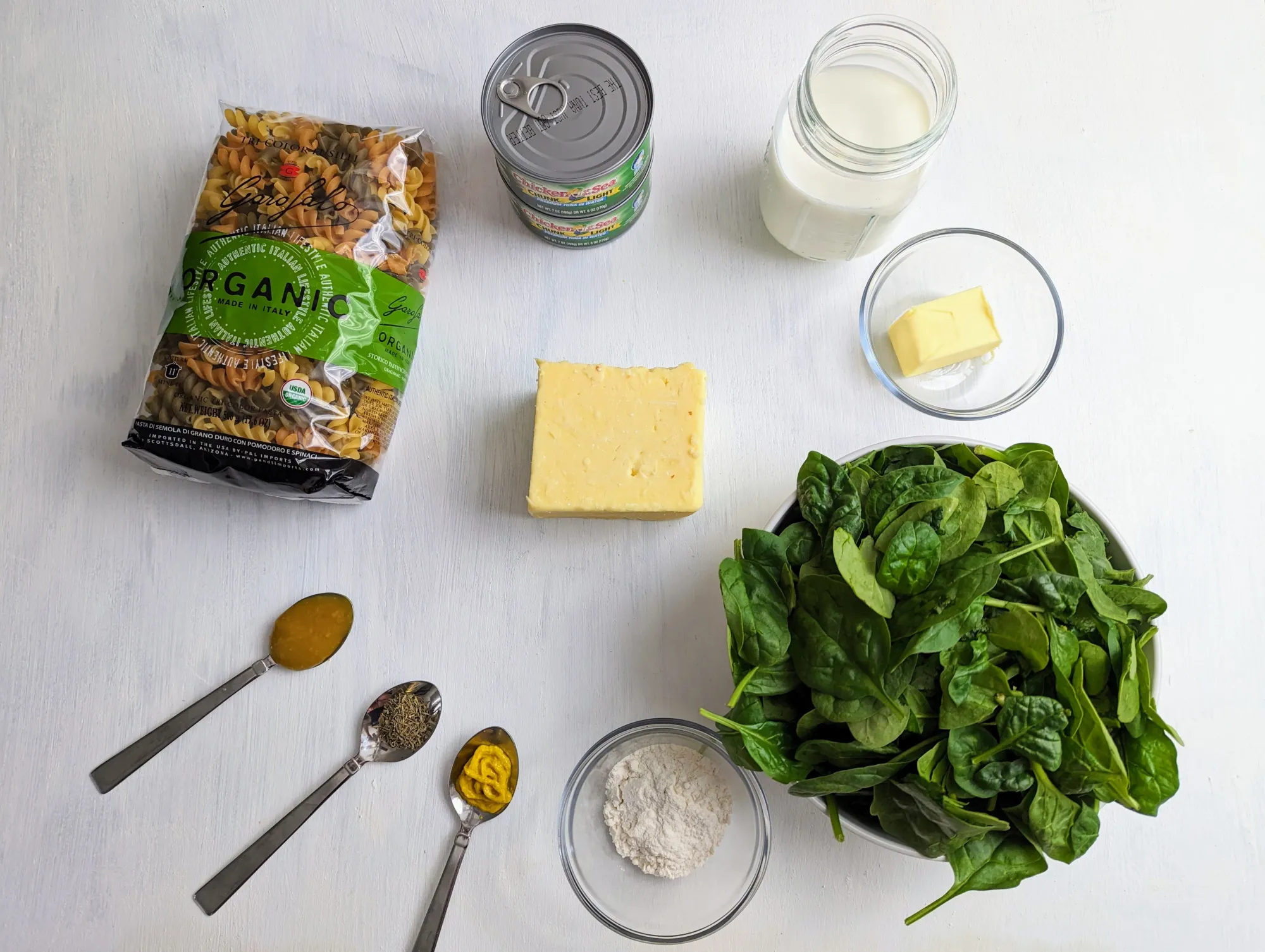 An image of the ingredients; pasta, canned tuna, milk, butter, spinach, flour, mustard, thyme, chicken bouillon and cheese.