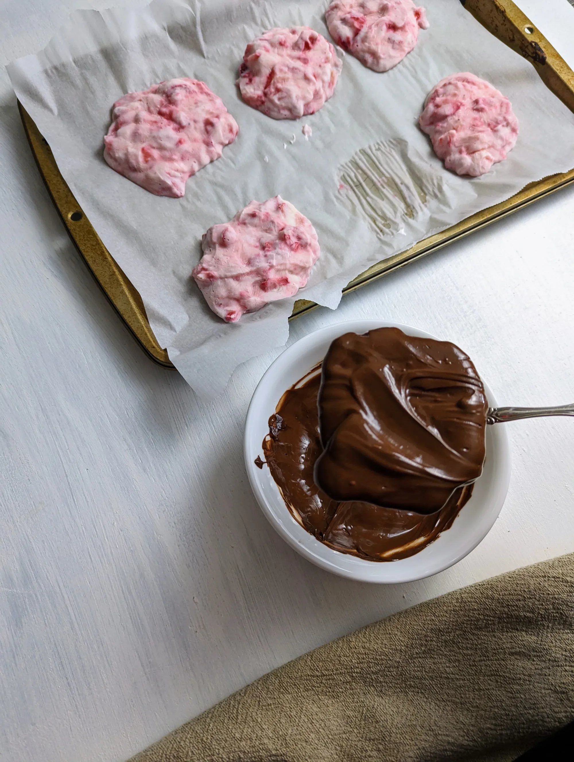 A dipped yogurt bite on a spoon, over a bowl of melted chocolaate