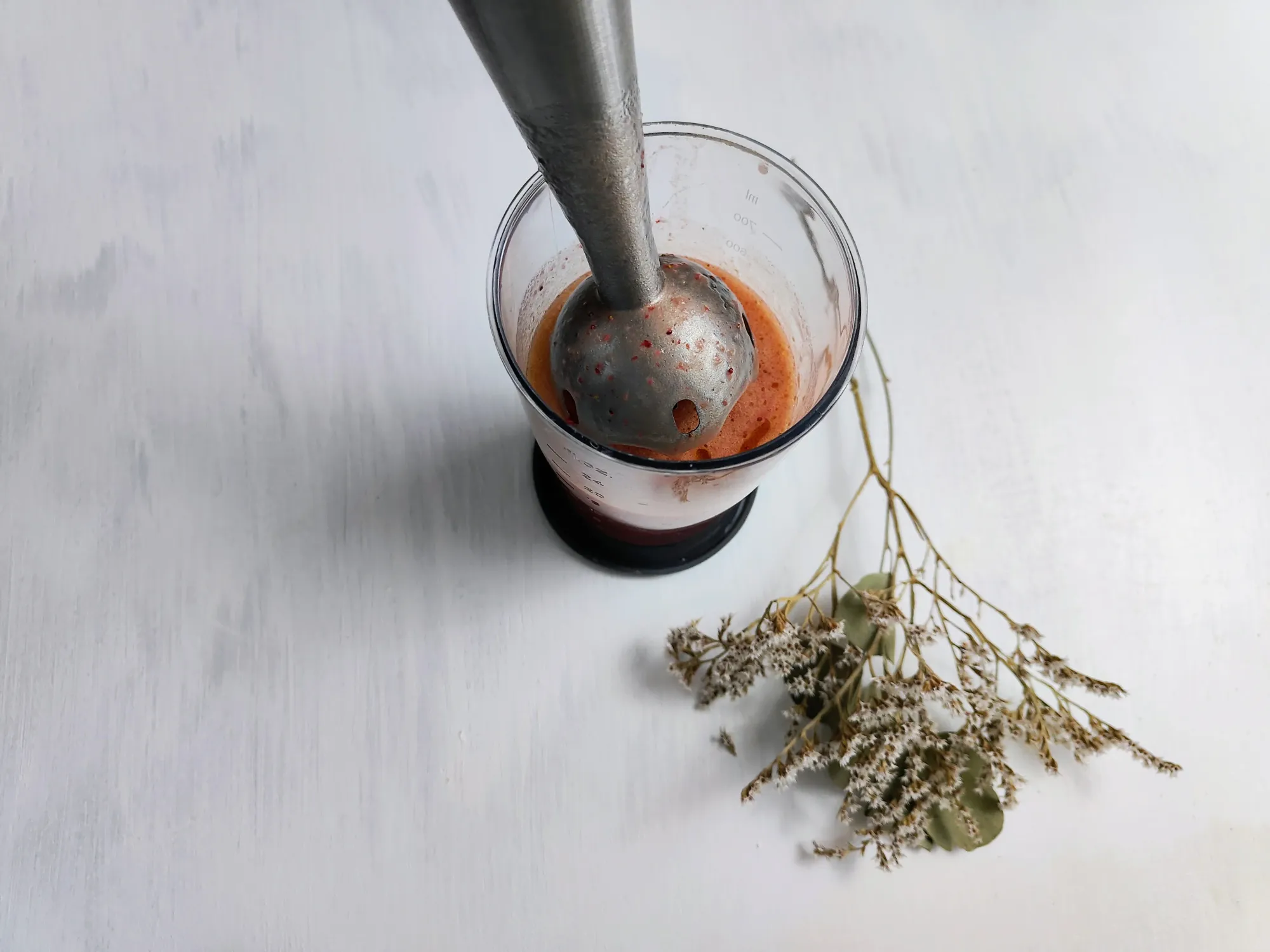 A cup of strawberry-flecked liquid with an immersion blender