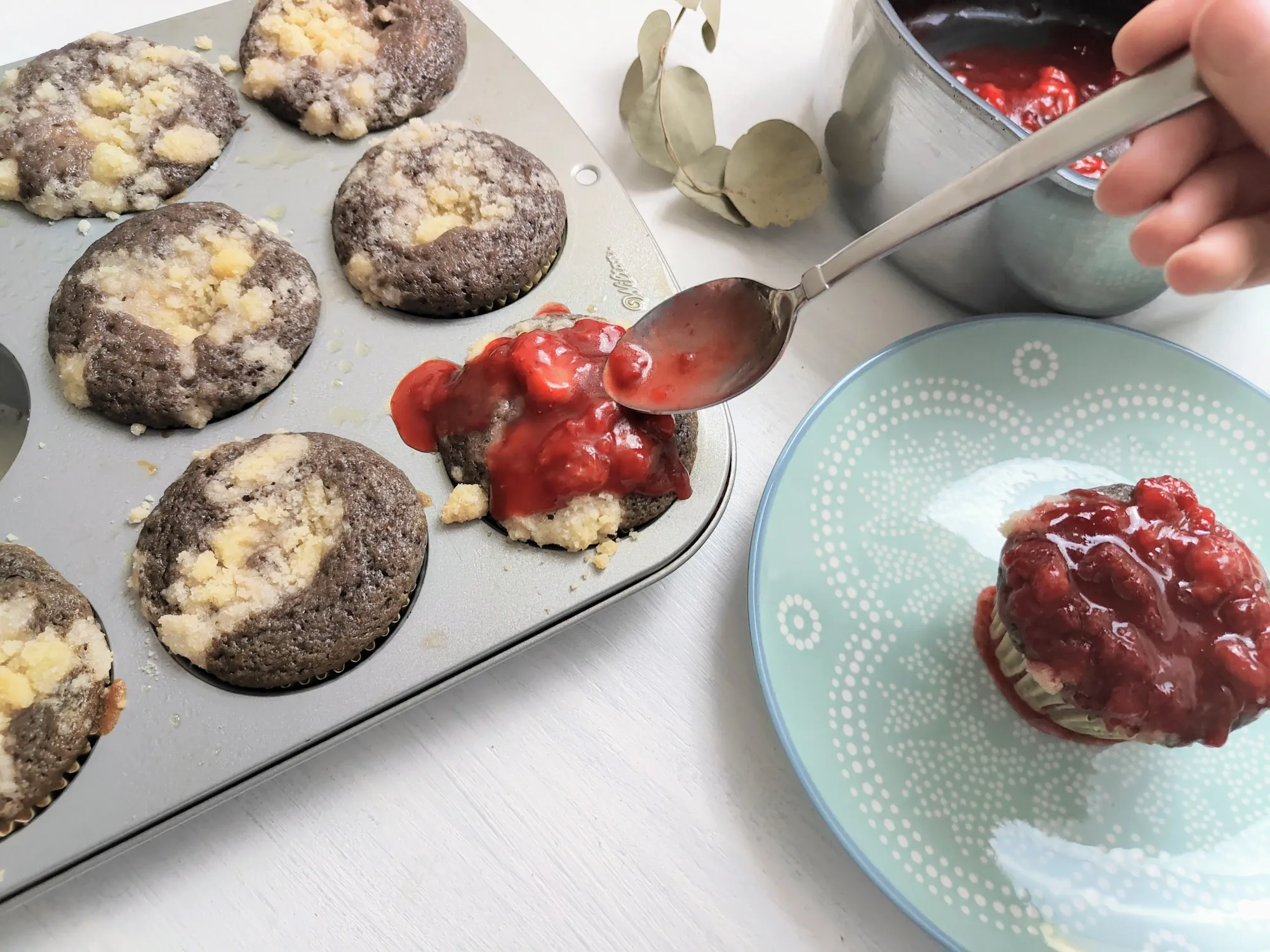 Muffins in a muffin tin being topped with strawberry syrup