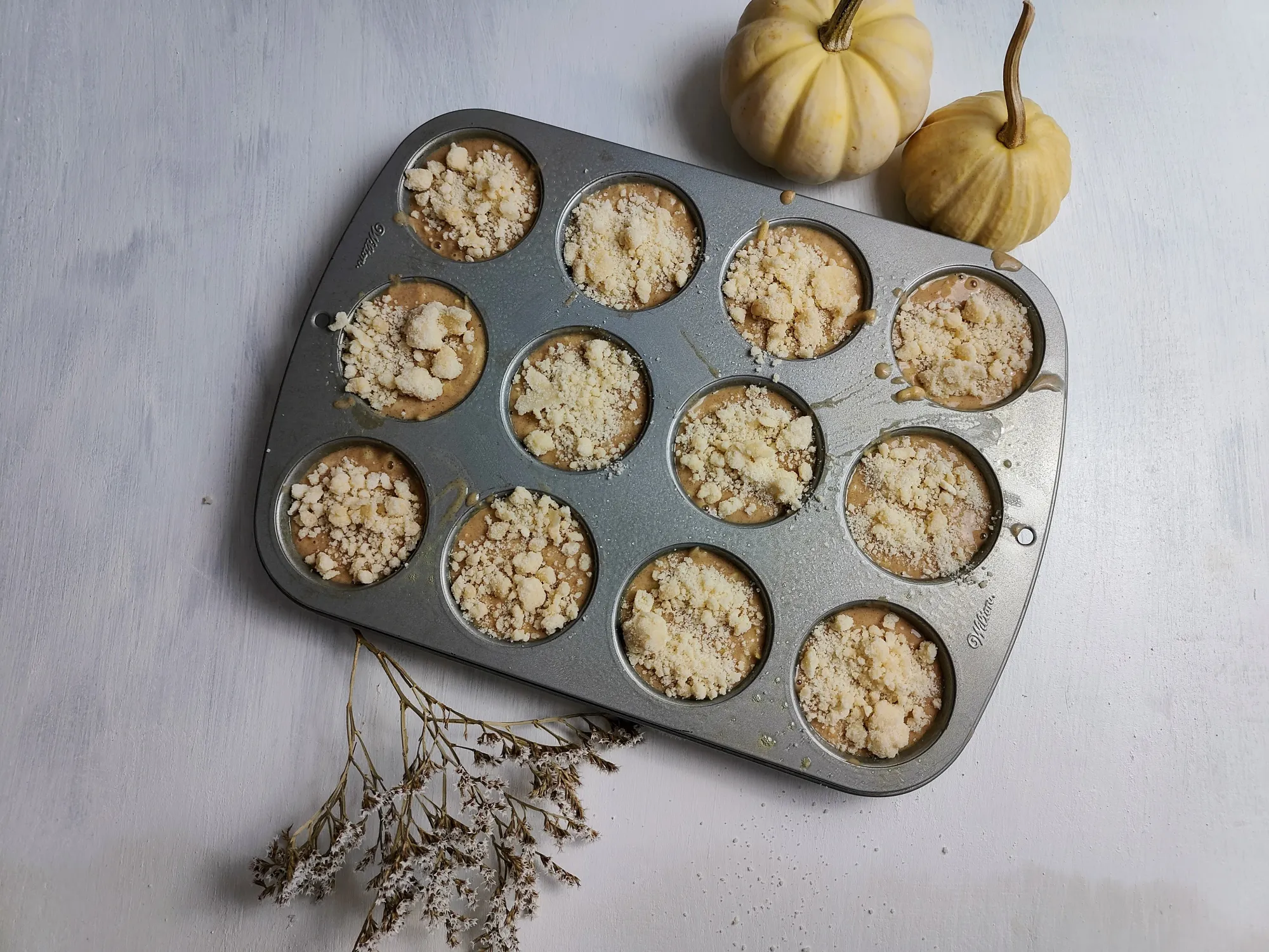 Muffin batter in a muffin tin topped with streusel