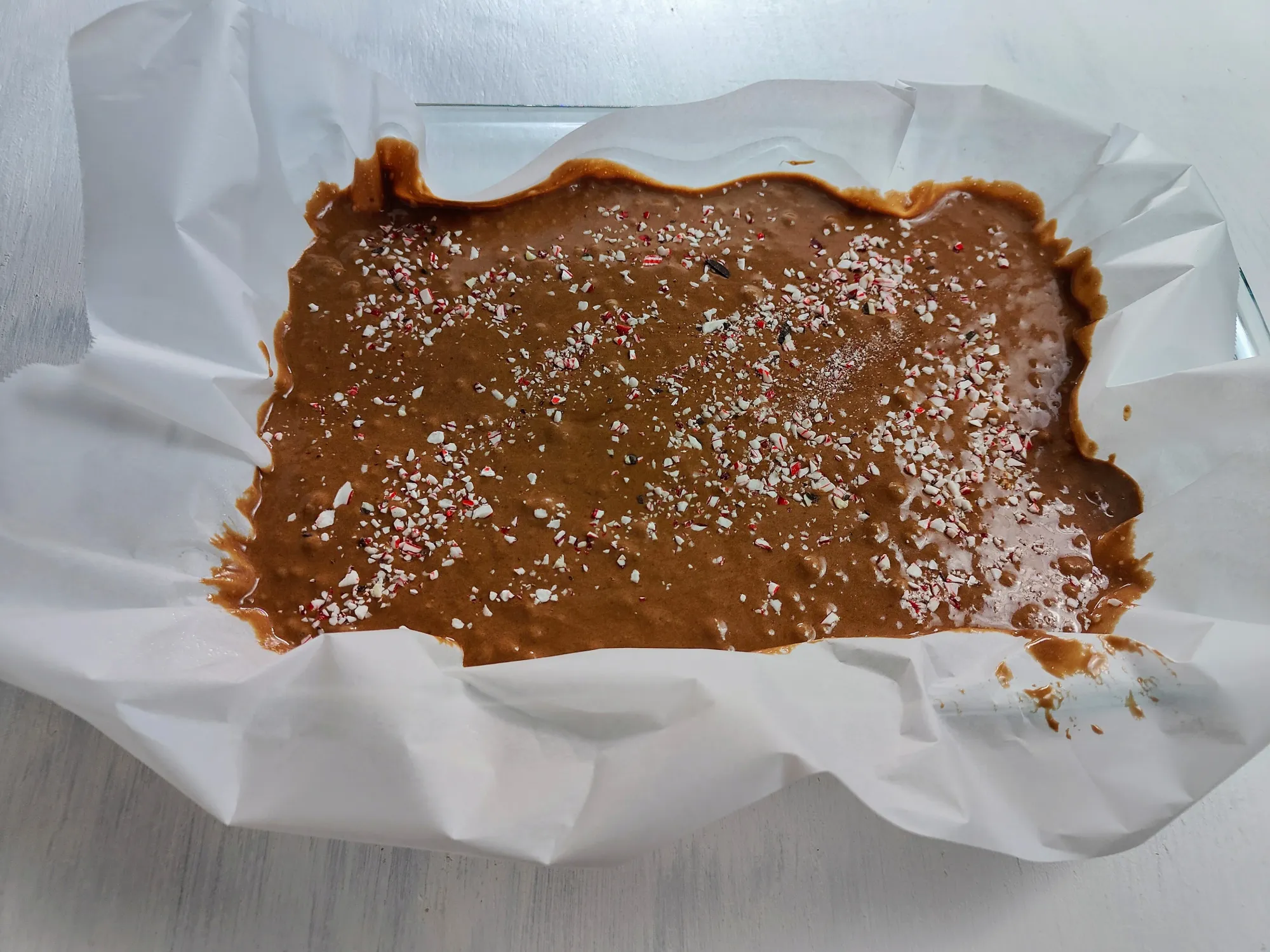 Brownie batter topped with crushed candy canes in baking paper lined dish