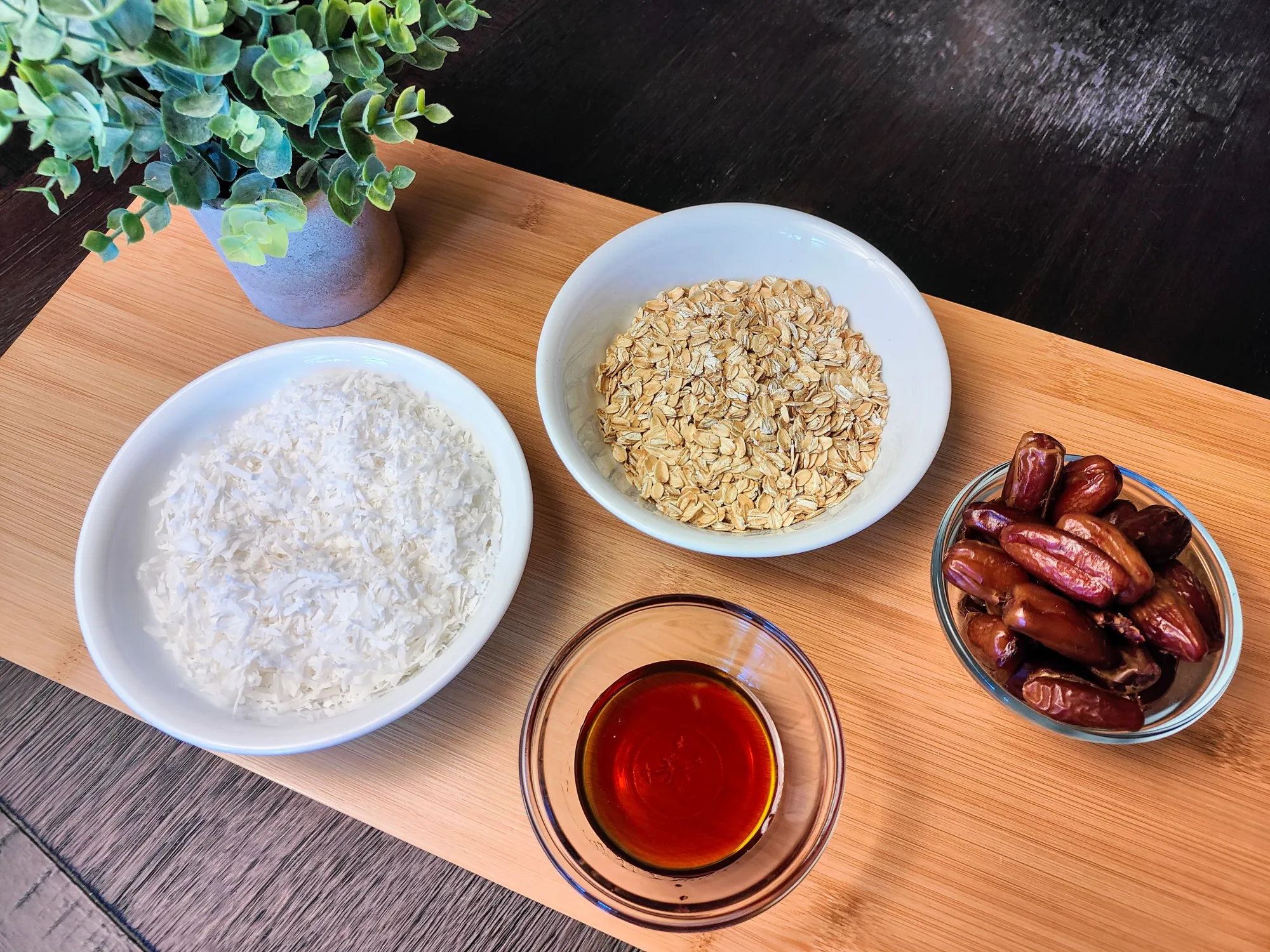 Dates, oats, coconut, and maple syrup in bowls on a cutting board