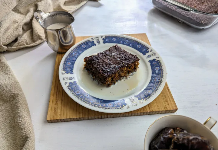 Sticky date pudding on a plate, covered in date infused milk with a small pitcher of milk next to it