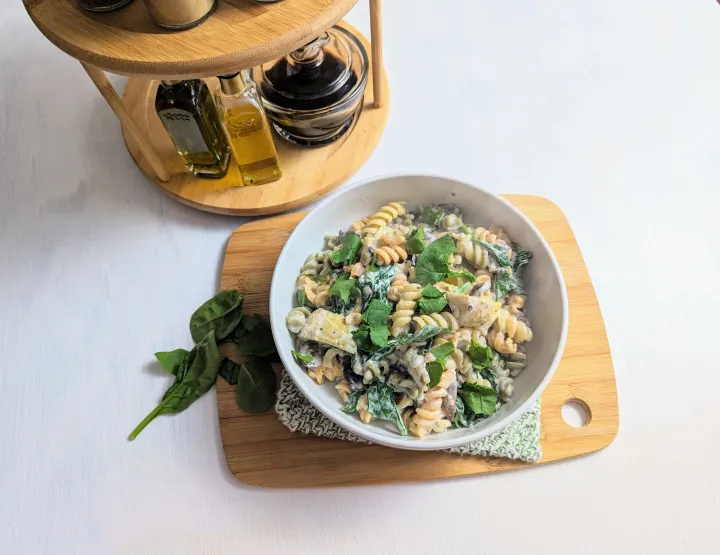 A bowl of pasta with spinach, mushrooms, artichokes, and a creamy sauce. 