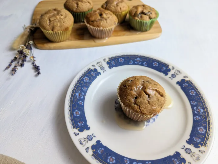 A glazed muffin on a plate, with more muffins behind on a cutting board.