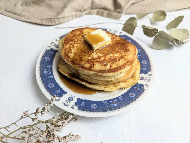 A stack of pancakes on a plate with butter and maple syrup