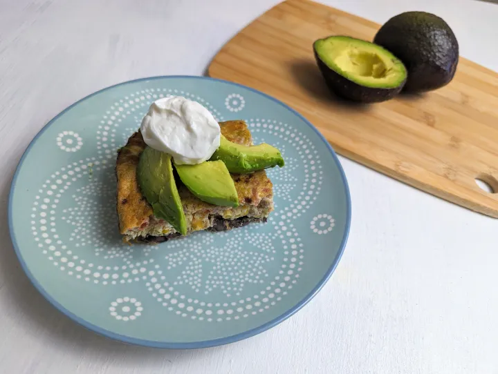 A slice of egg casserole topped with avocado and greek yogurt