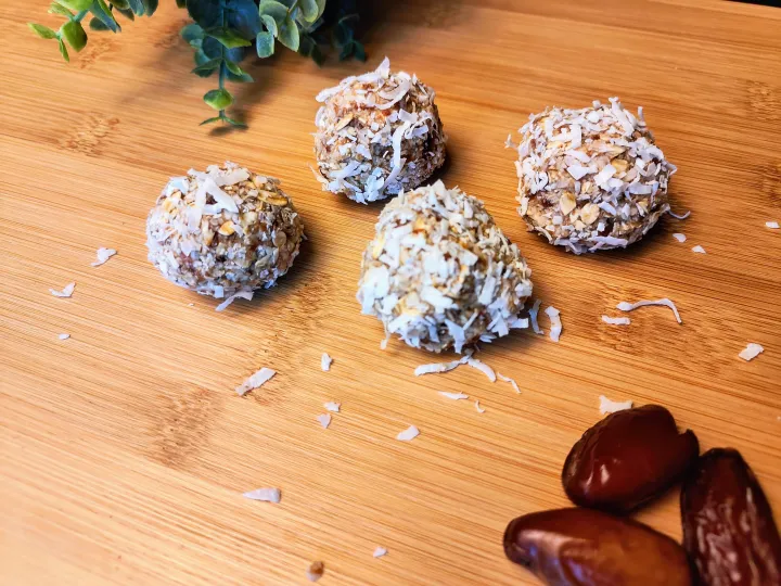 coconut coated oat and date balls on a cutting board with more dates